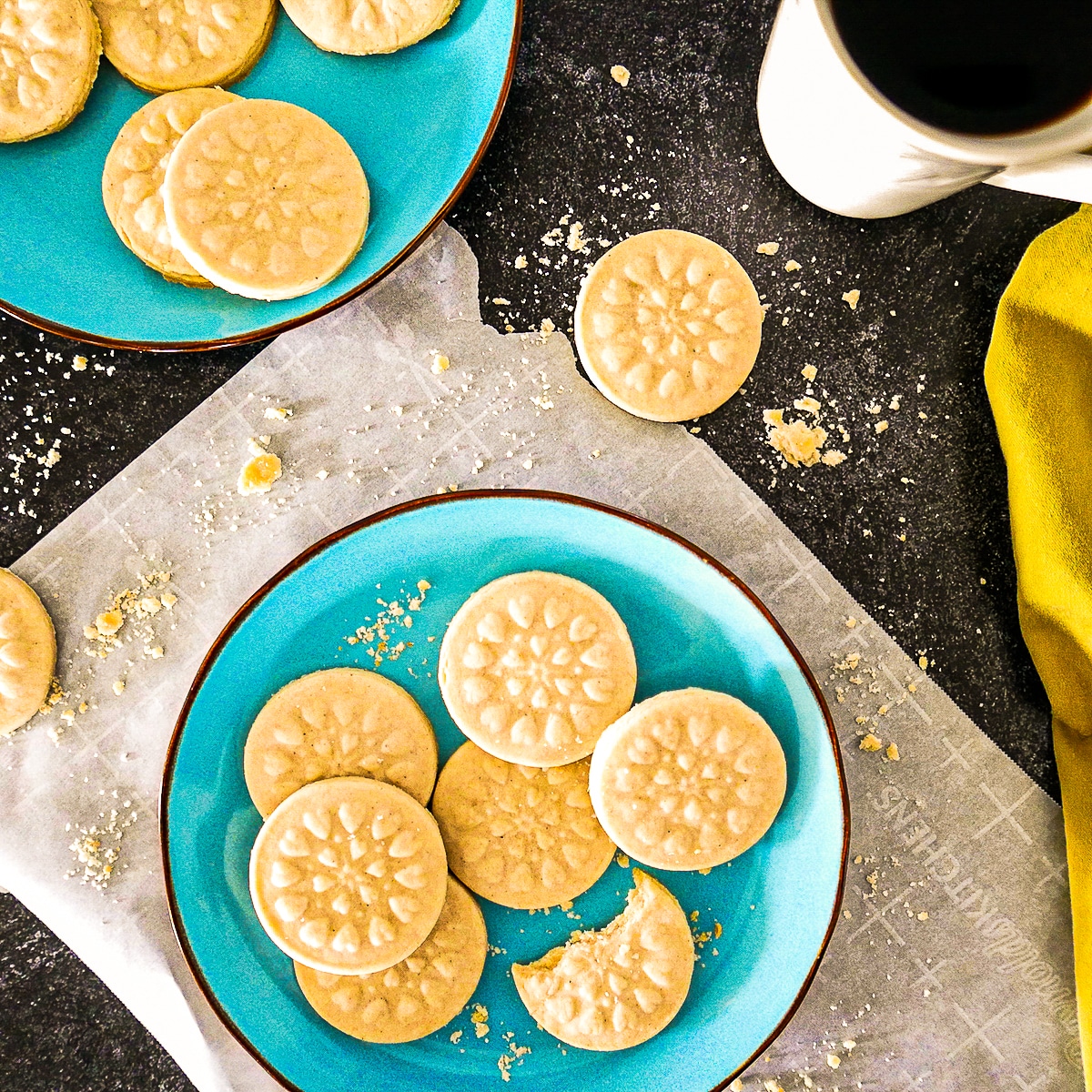 Rich and buttery cardamom shortbread cookies arranged on two blue plates with a cup of coffee.