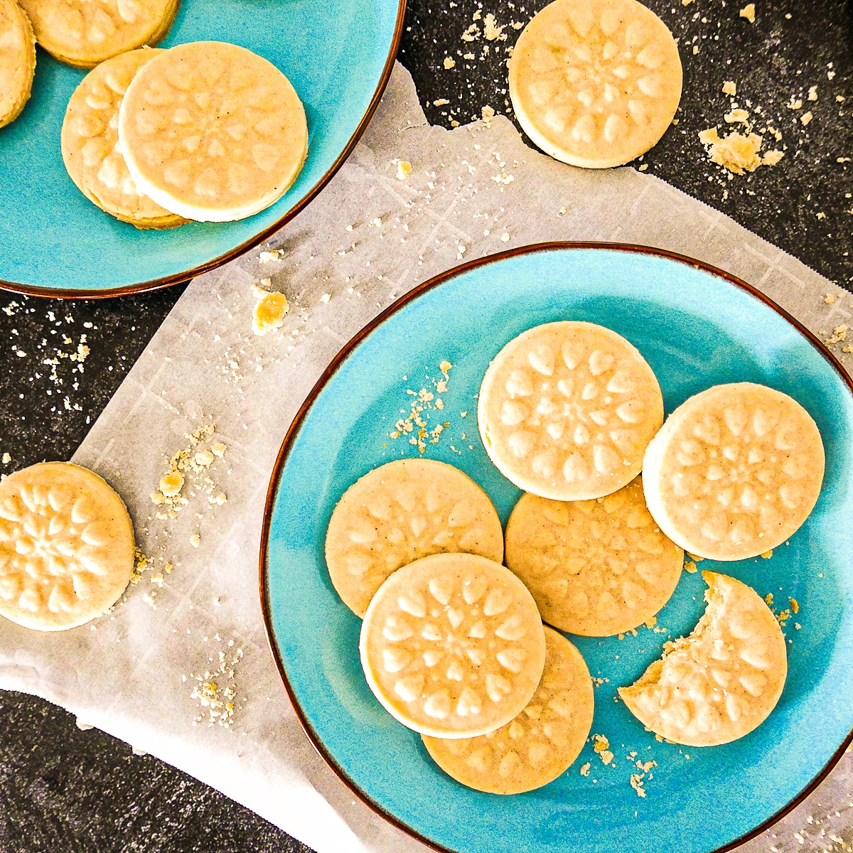 Buttery cardamom shortbread arranged on a plate with cookie crumbs.