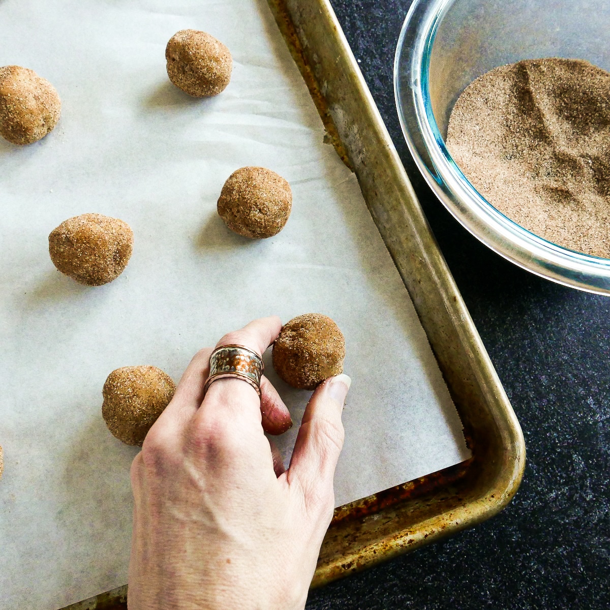 Rolling cookie dough balls into cinnamon-sugar mixture.