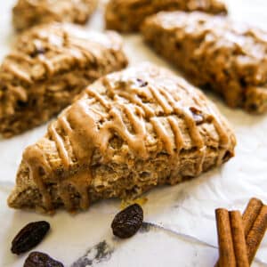 Soft and tender cinnamon raisin scones with a sweet glaze arranged on parchment paper.