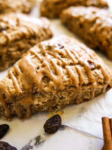 Soft and tender cinnamon raisin scones with a sweet glaze arranged on parchment paper.