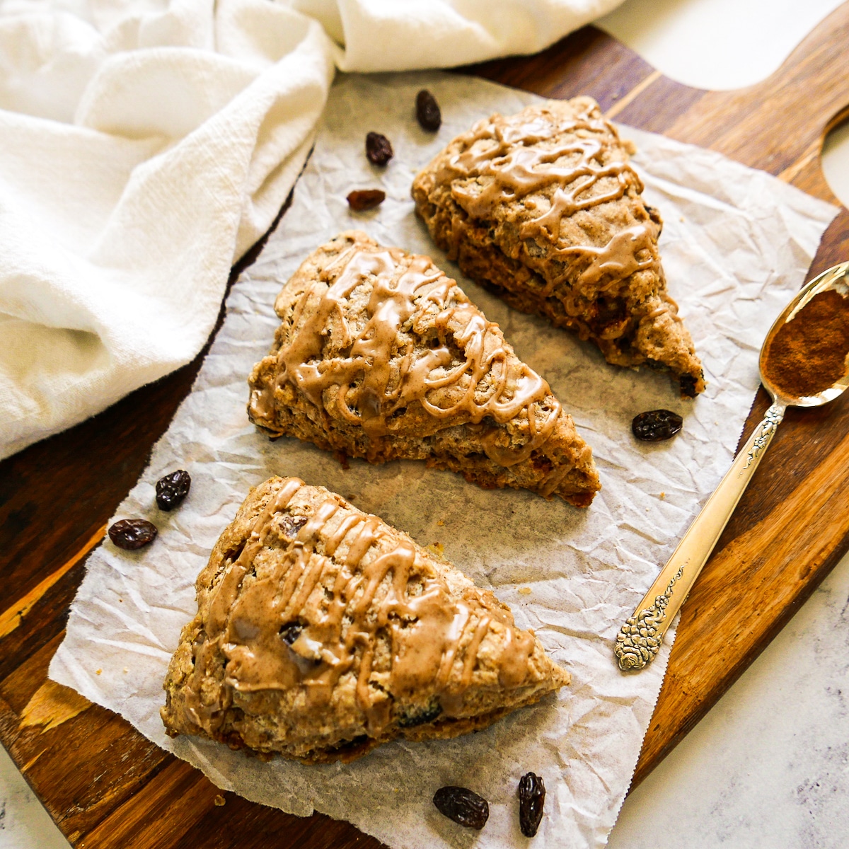 three cinnamon raisin scones arranged on a wooden board with plump raisins. 