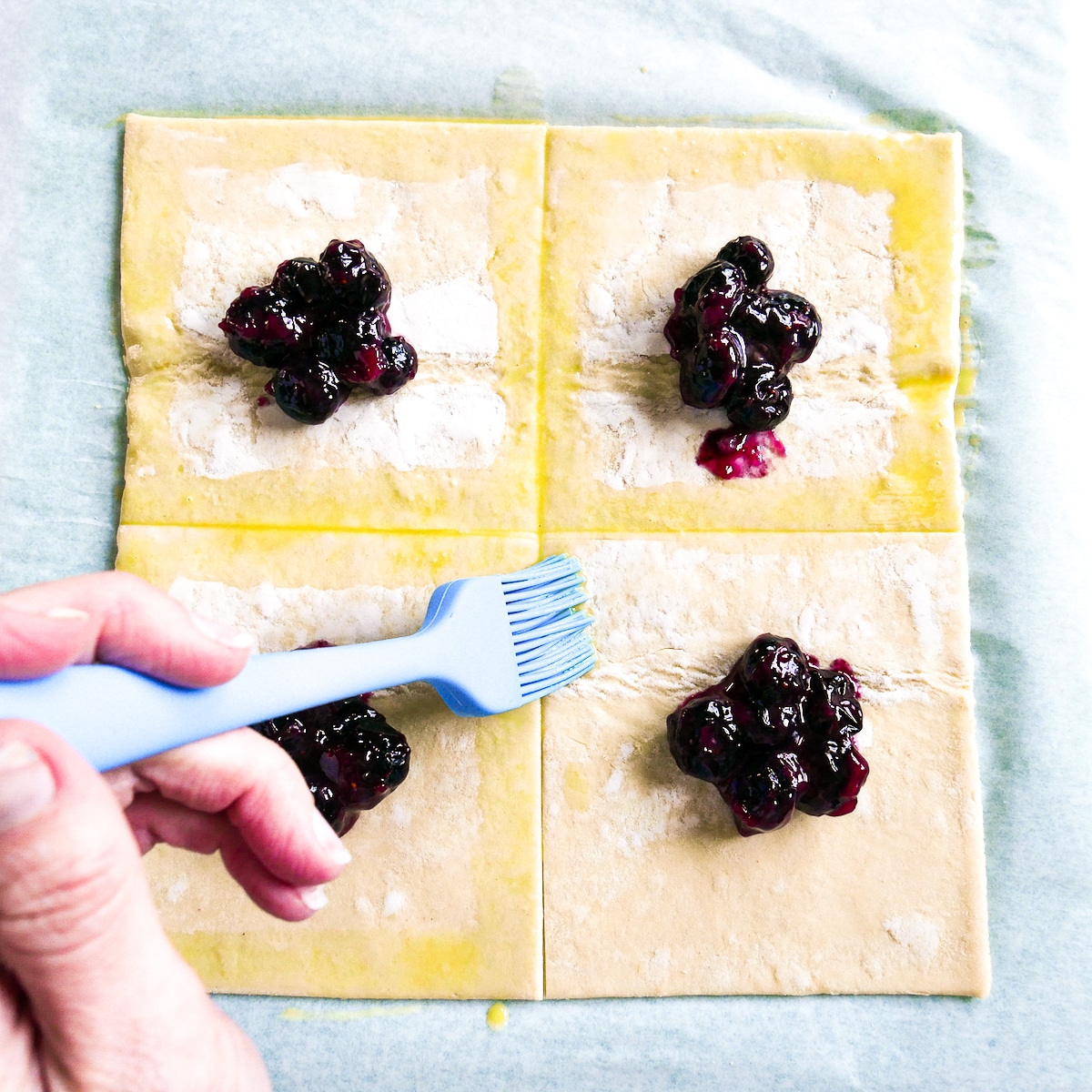 Puff pastry squares being brushed with egg wash.