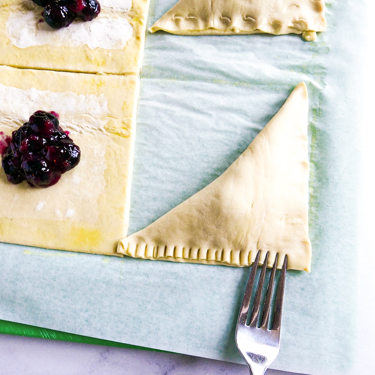 Crimping puff pastry triangles on a cutting board.