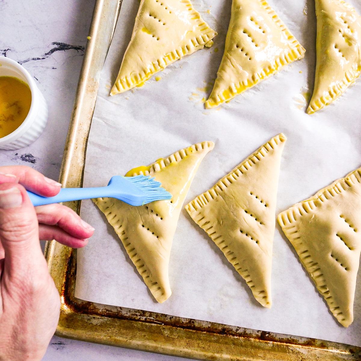 Hand brushing egg wash onto top of blueberry turnovers.