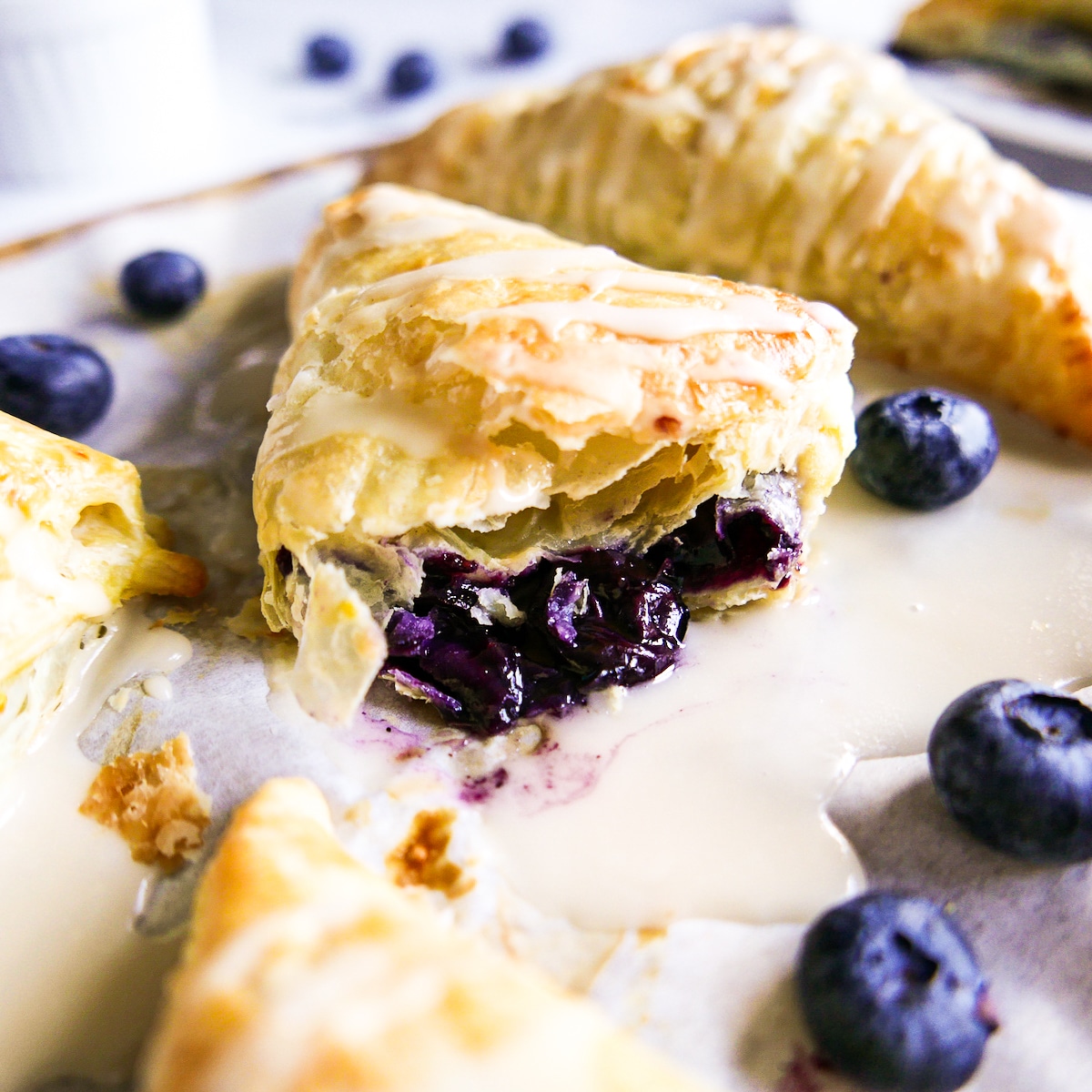 Puff pastry blueberry turnover cut in half with fresh blueberries next to it.