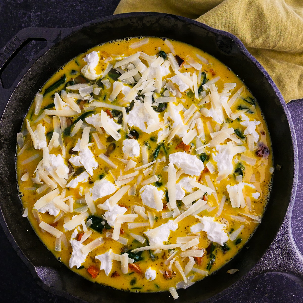 Assembled frittata sprinkled with crumbled goat cheese and Parmesan.