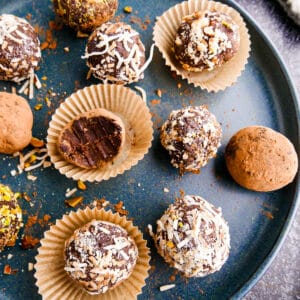 Creamy vegan truffles arranged on a white plate with cup of chocolate in background.