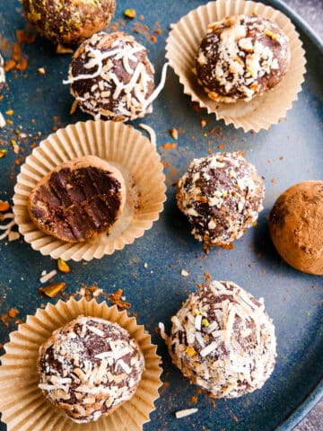 Creamy vegan truffles arranged on a white plate with cup of chocolate in background.