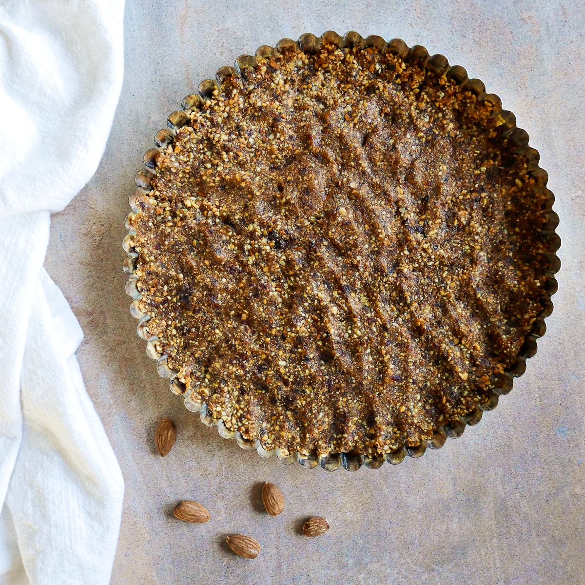 tart crust pressed into tart pan with a few almonds next to it. 