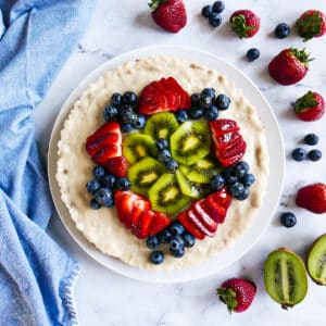 vegan fruit tart with kiwi and berries on a platter and surrounded by more berries.