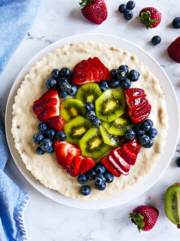 vegan fruit tart with kiwi and berries on a platter and surrounded by more berries.