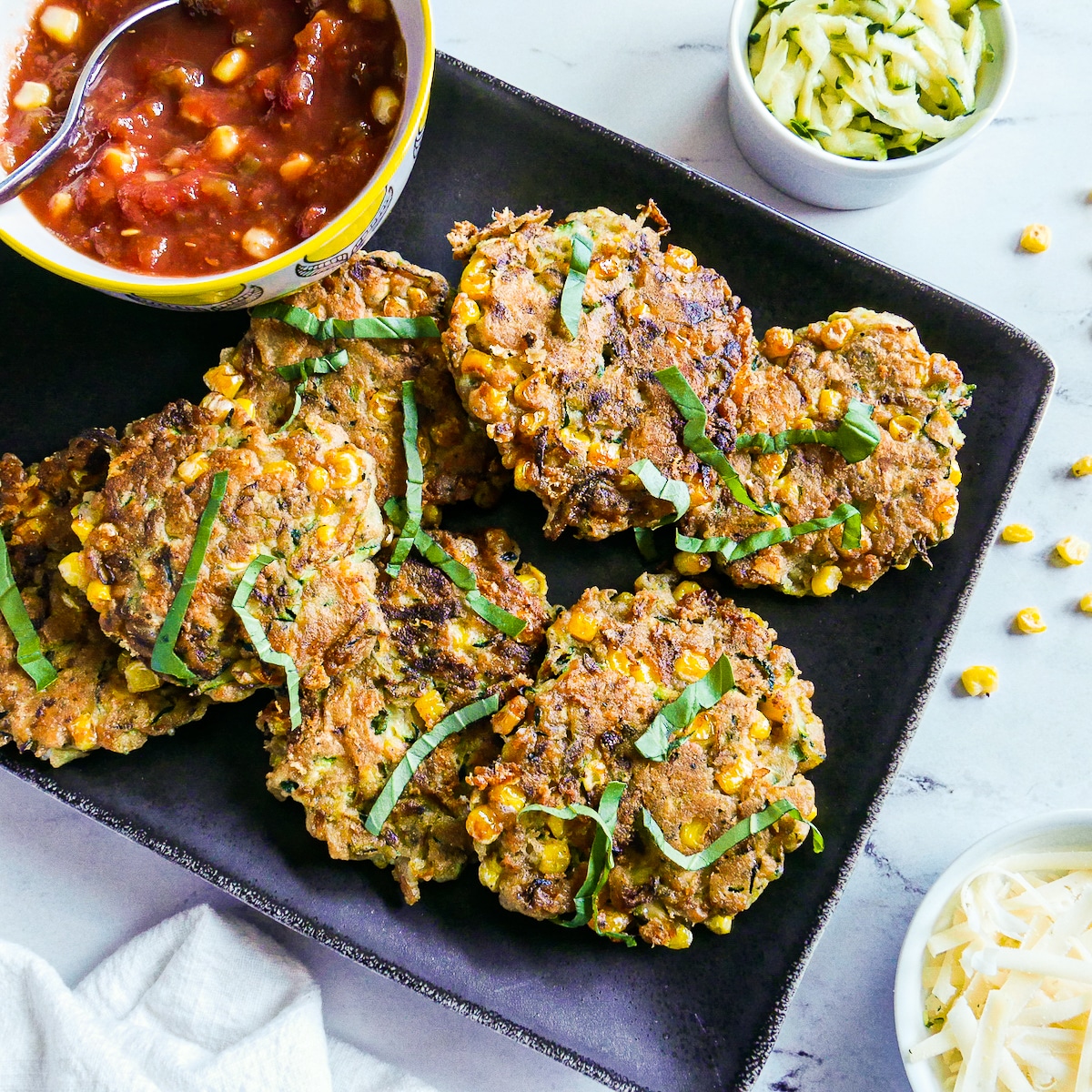 Zucchini fritters with corn arranged on a black platter with salsa.