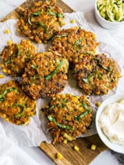 Zucchini and corn fritters arranged on parchment paper with a cup of sauce.