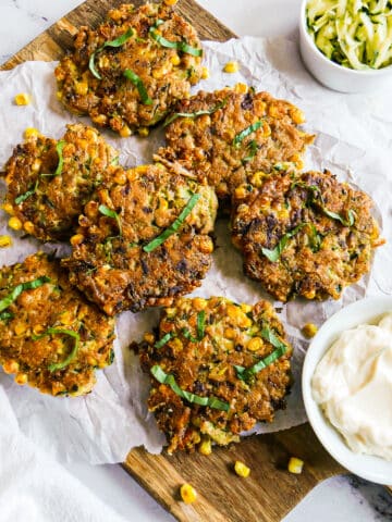 Zucchini and corn fritters arranged on parchment paper with a cup of sauce.