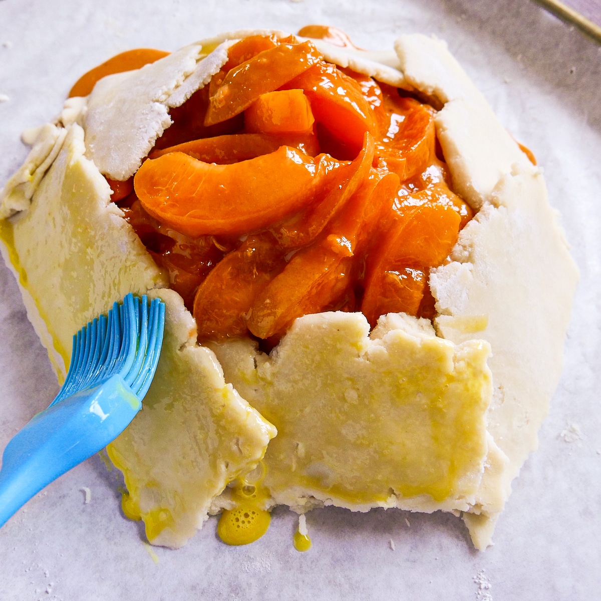 Brushing egg wash on galette dough with a pastry brush.