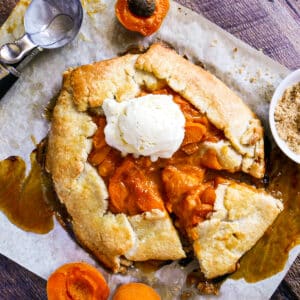 Sliced apricot galette on a baking sheet topped with a scoop of vanilla ice cream.
