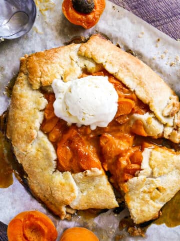 Sliced apricot galette on a baking sheet topped with a scoop of vanilla ice cream.