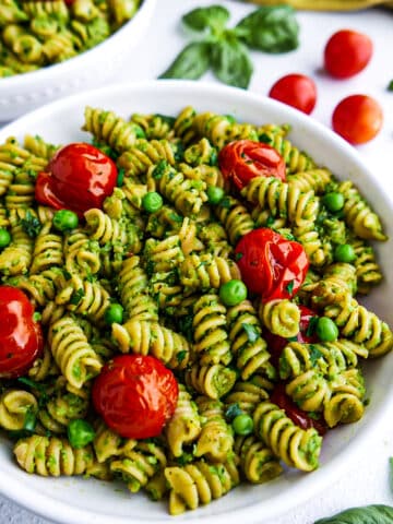 Creamy pesto pasta with roasted tomatoes in a white bowl.