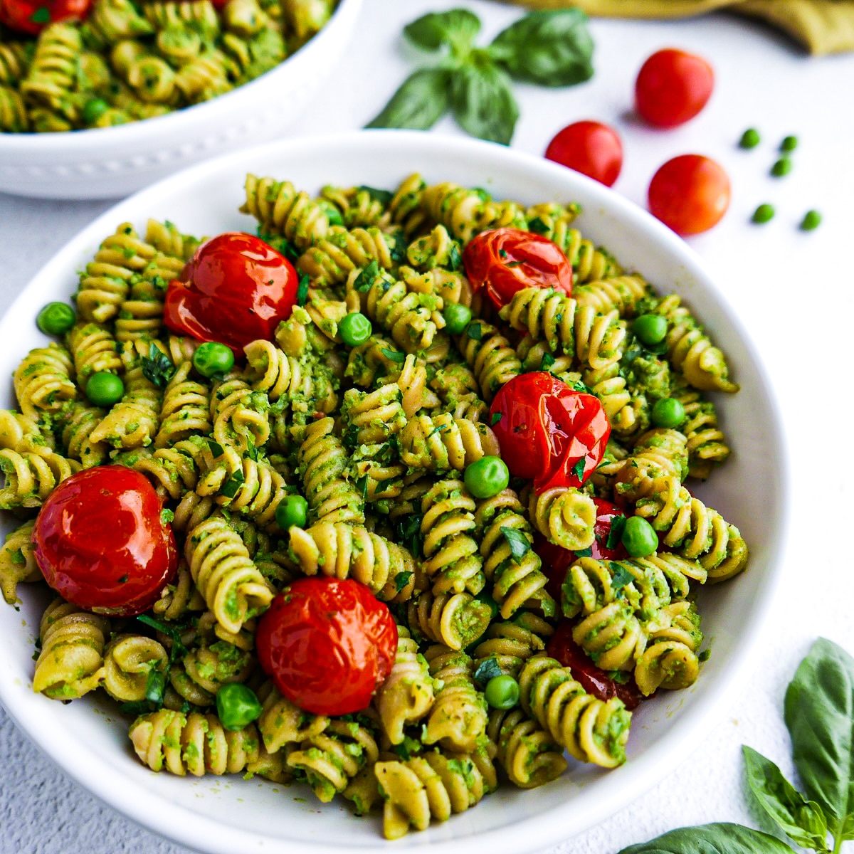 Creamy pesto pasta with roasted tomatoes in a white bowl.