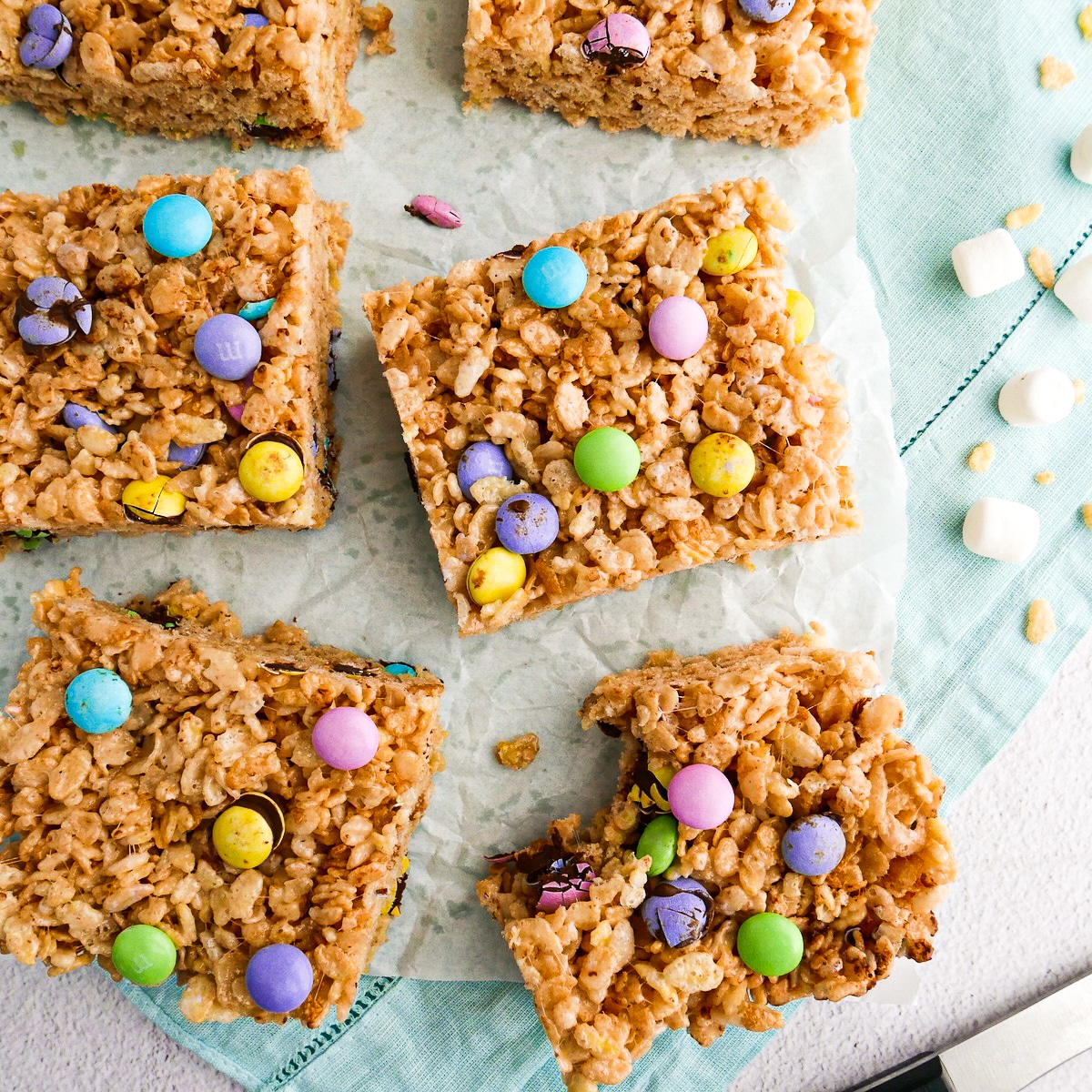 Soft and chewy rice krispie treats with m&m's arranged on parchment.