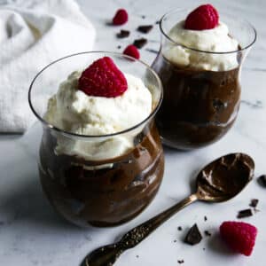 Two glass cups with avocado chocolate mousse and topped with whipped cream.