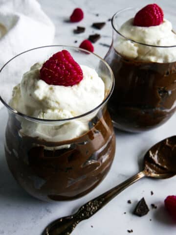 Two glass cups with avocado chocolate mousse and topped with whipped cream.