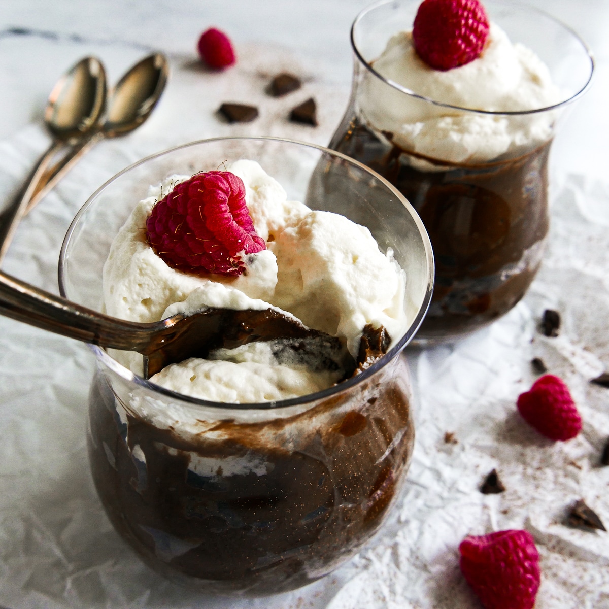 Two cups of chocolate pudding with two spoons in the background.