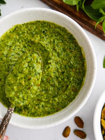 Creamy pistachio pesto in a bowl with a spoon.