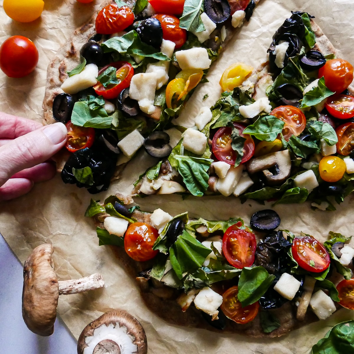 Hand picking up slice of baked flatbread pizza from table.