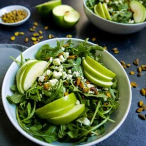 Bowl of crisp apple and pistachio salad with pistachios sprinkled around.