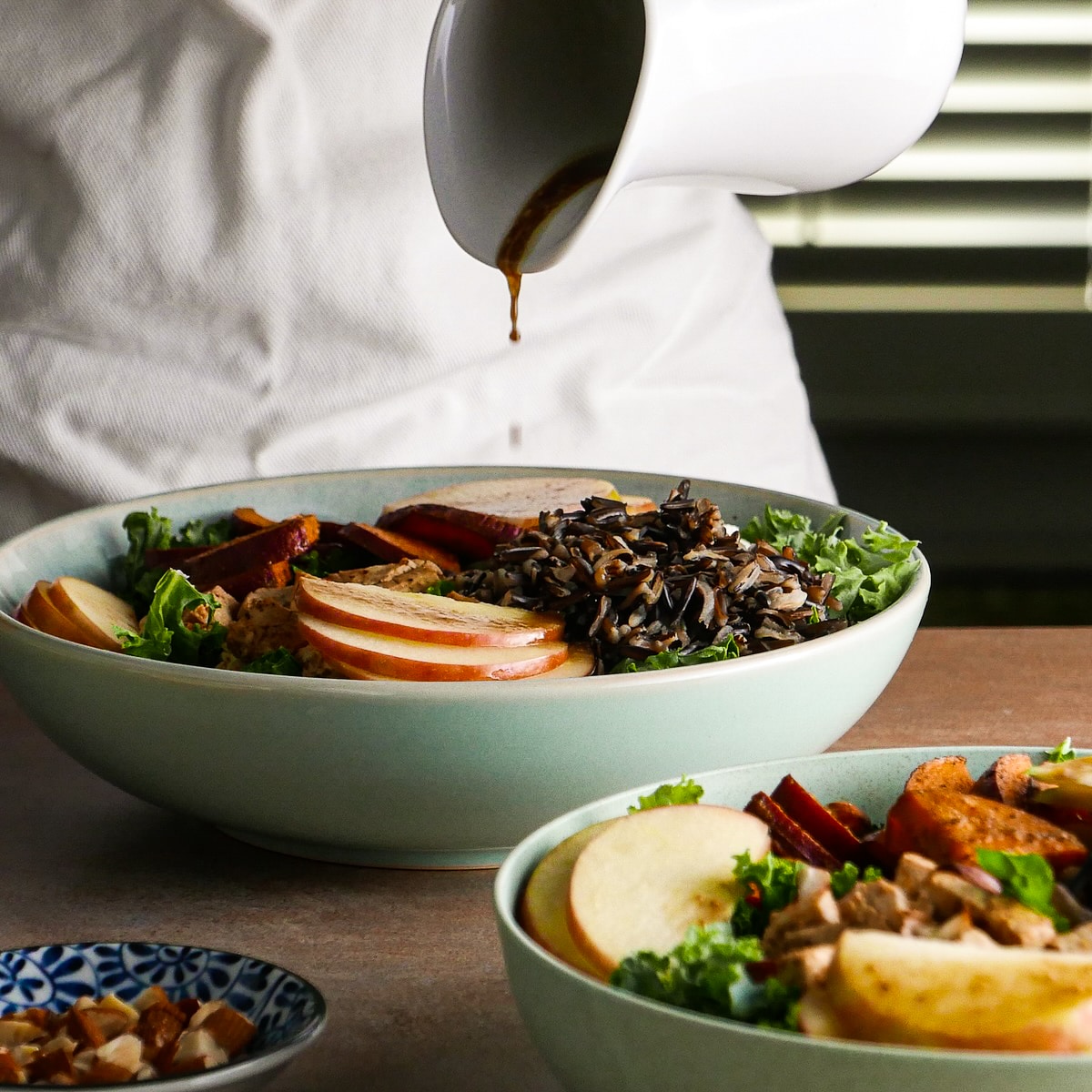 Drizzling balsamic dressing onto creamy and crunchy fall salad.