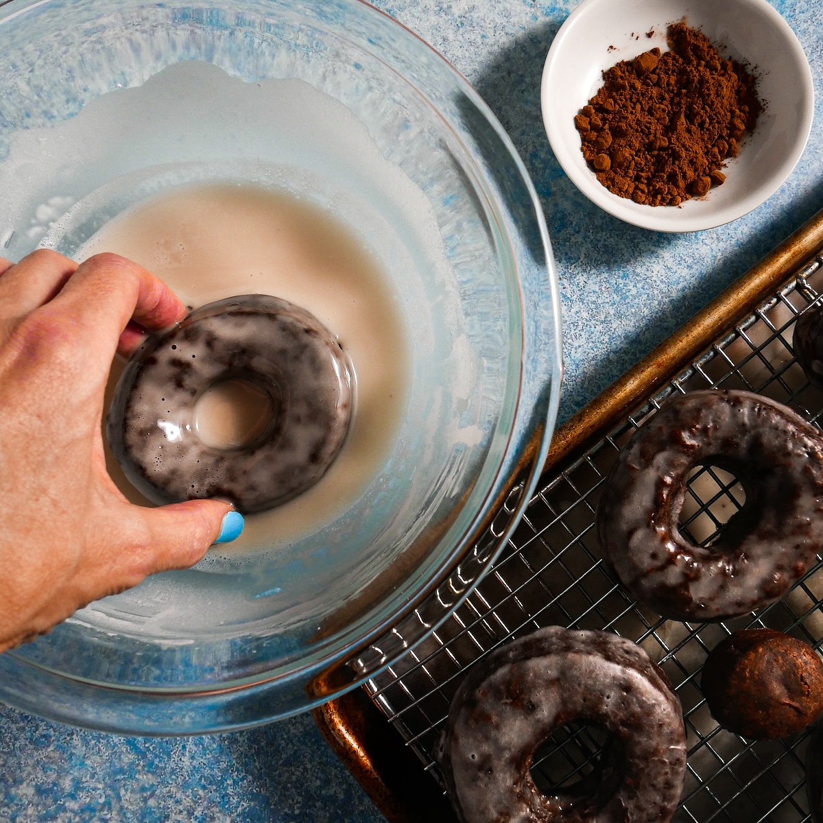 Dipping warm donuts into a bowl of vanilla glaze.