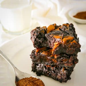 Fudgy vegan pumpkin brownies stacked on a white plate.