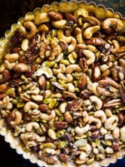 Mixed nut tart on a white platter with gingham napkin and rolling pin.