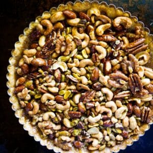 Mixed nut tart on a white platter with gingham napkin and rolling pin.