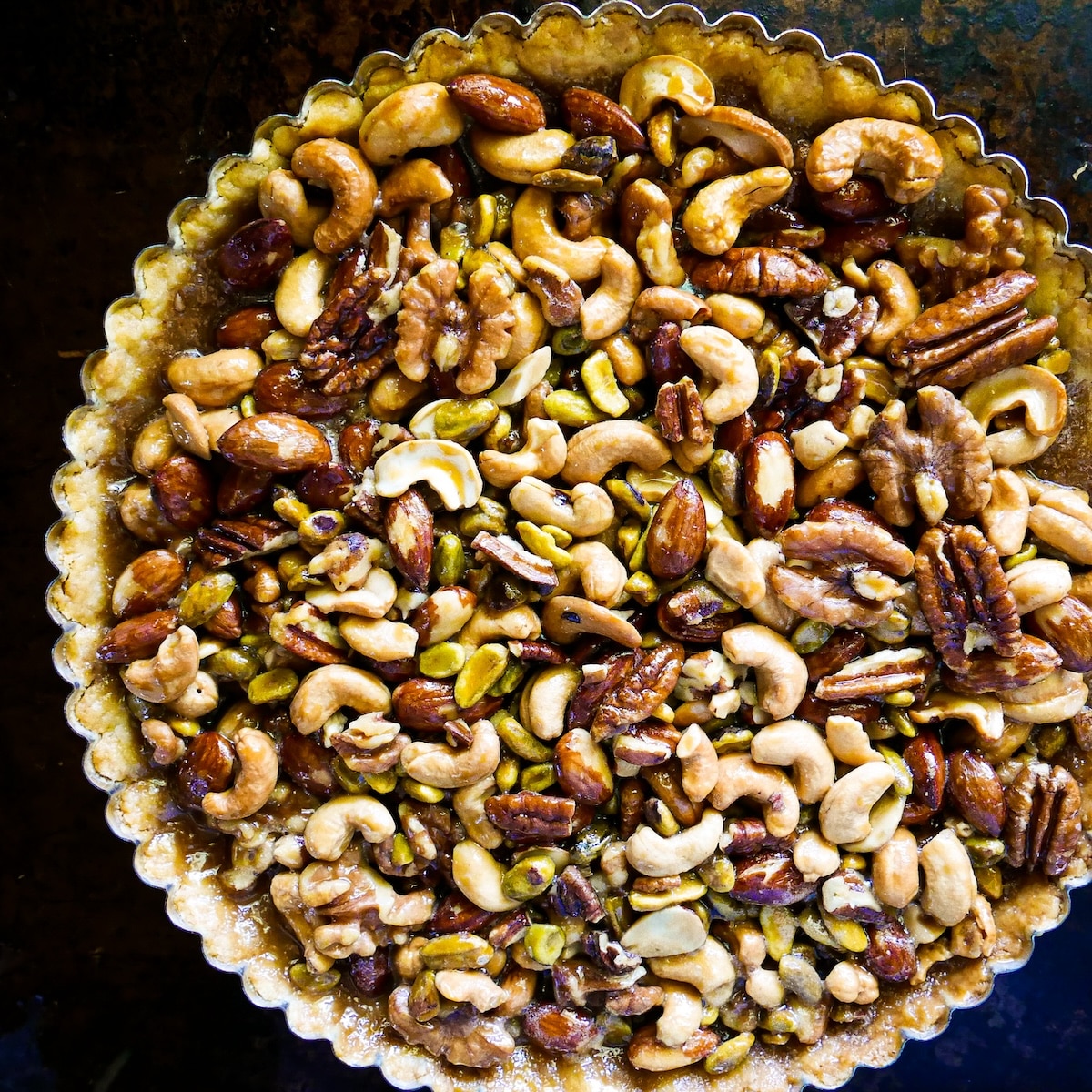 caramel-nut-tart.jpg Mixed nut tart on a white platter with gingham napkin and rolling pin.