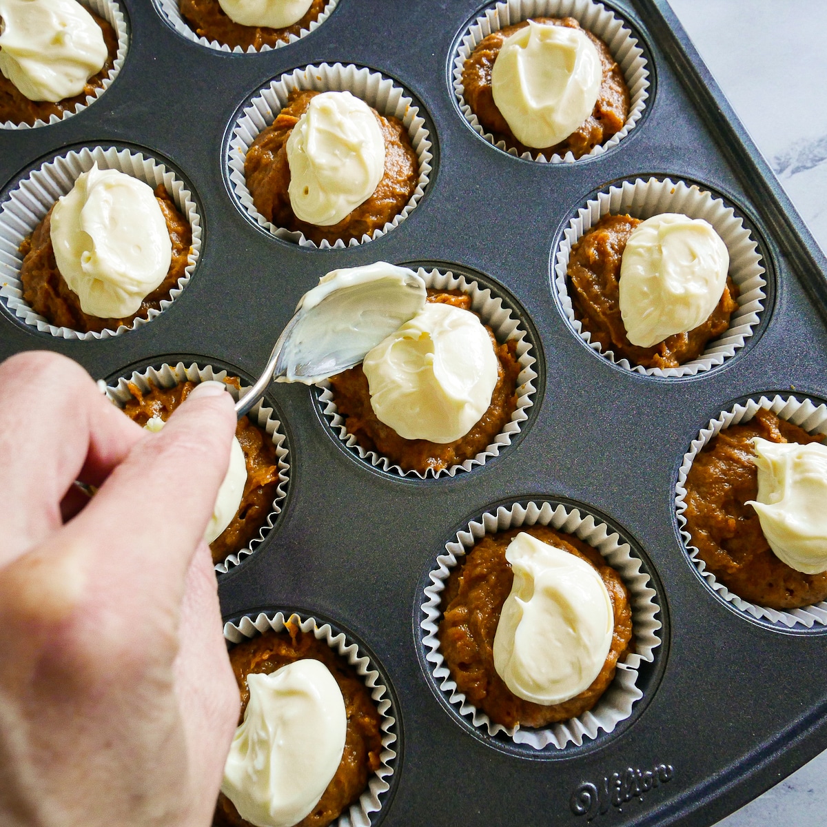 cream-cheese-on-muffins.jpg Placing a tablespoon of cream cheese mixture on top of muffin batter.