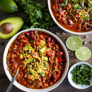 Two bowls of easy vegetarian chili surrounded by cilantro, avocado, and limes.