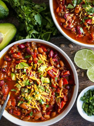 Two bowls of easy vegetarian chili surrounded by cilantro, avocado, and limes.