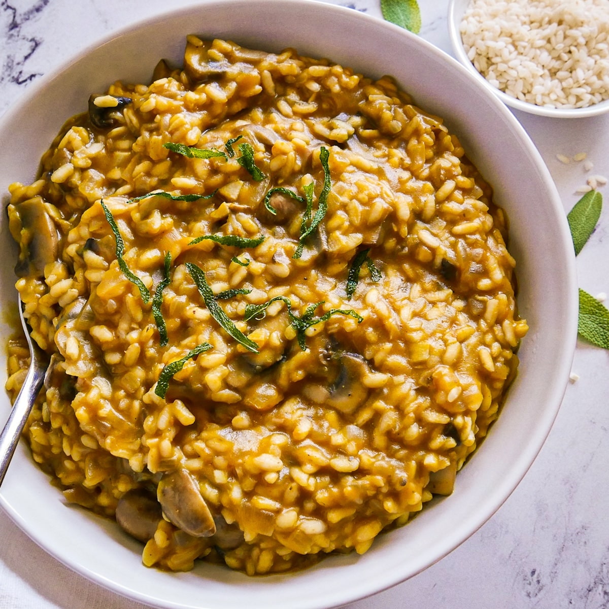 vegan-risotto.jpg bowl of vegan risotto with a spoon, white napkin, and sage leaves.
