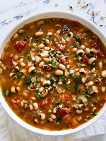 bowl of black eyed pea soup with a spoon and plate of bread.