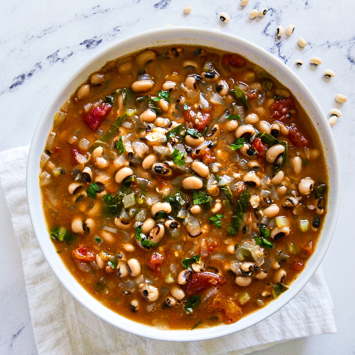 bowl of black eyed pea soup with a spoon and plate of bread.