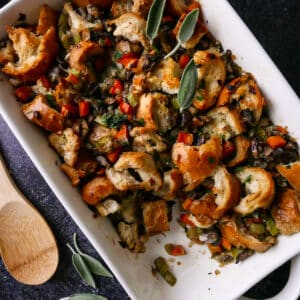 Mushroom dressing in a baking dish with a wooden spoon and sage next to dish.