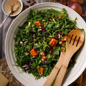 Roasted squash salad in a bowl with arugua, Parmesan cheese, and pecans.