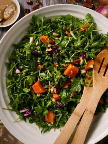 Roasted squash salad in a bowl with arugua, Parmesan cheese, and pecans.