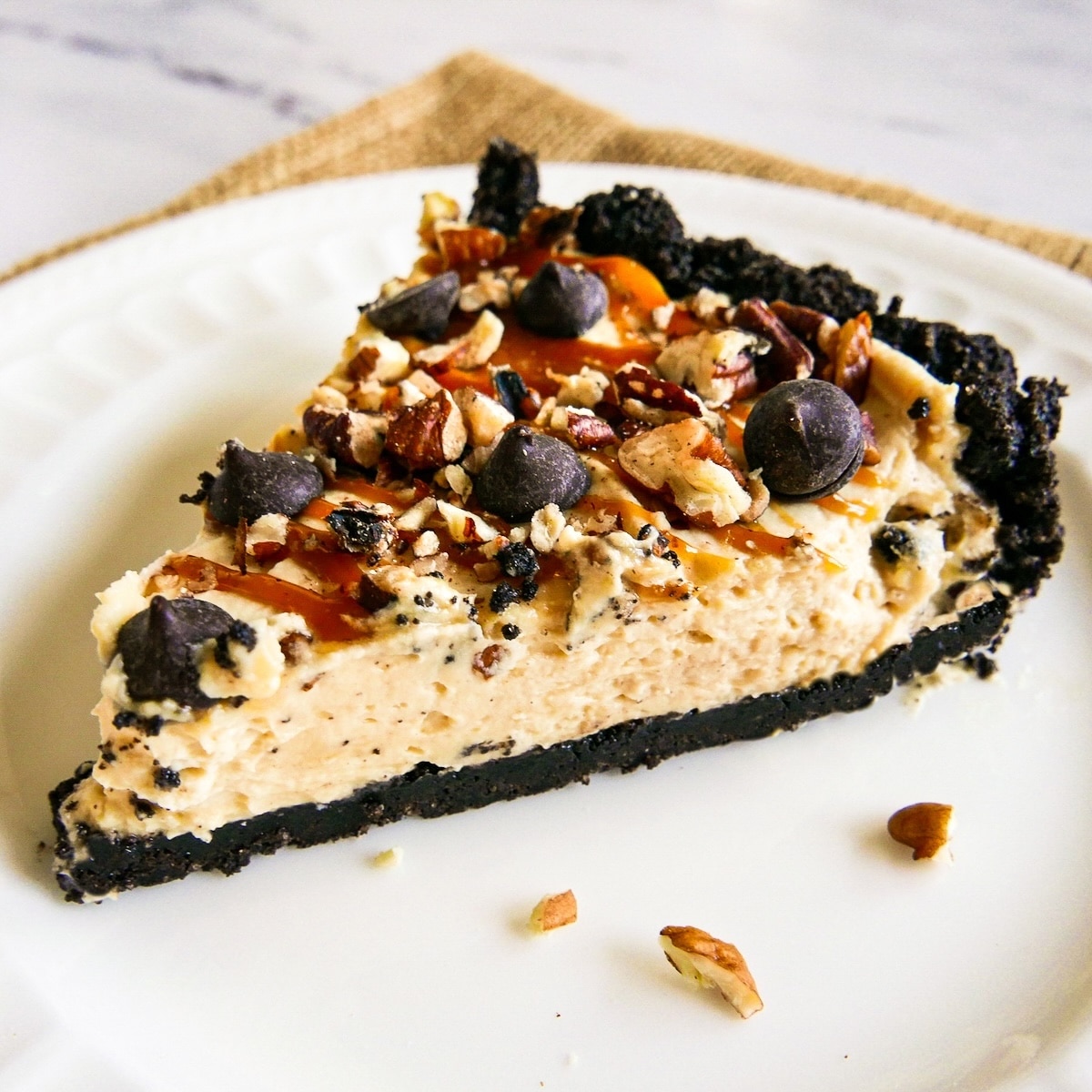 slice of pecan turtle pie on a white plate with chopped pecans.