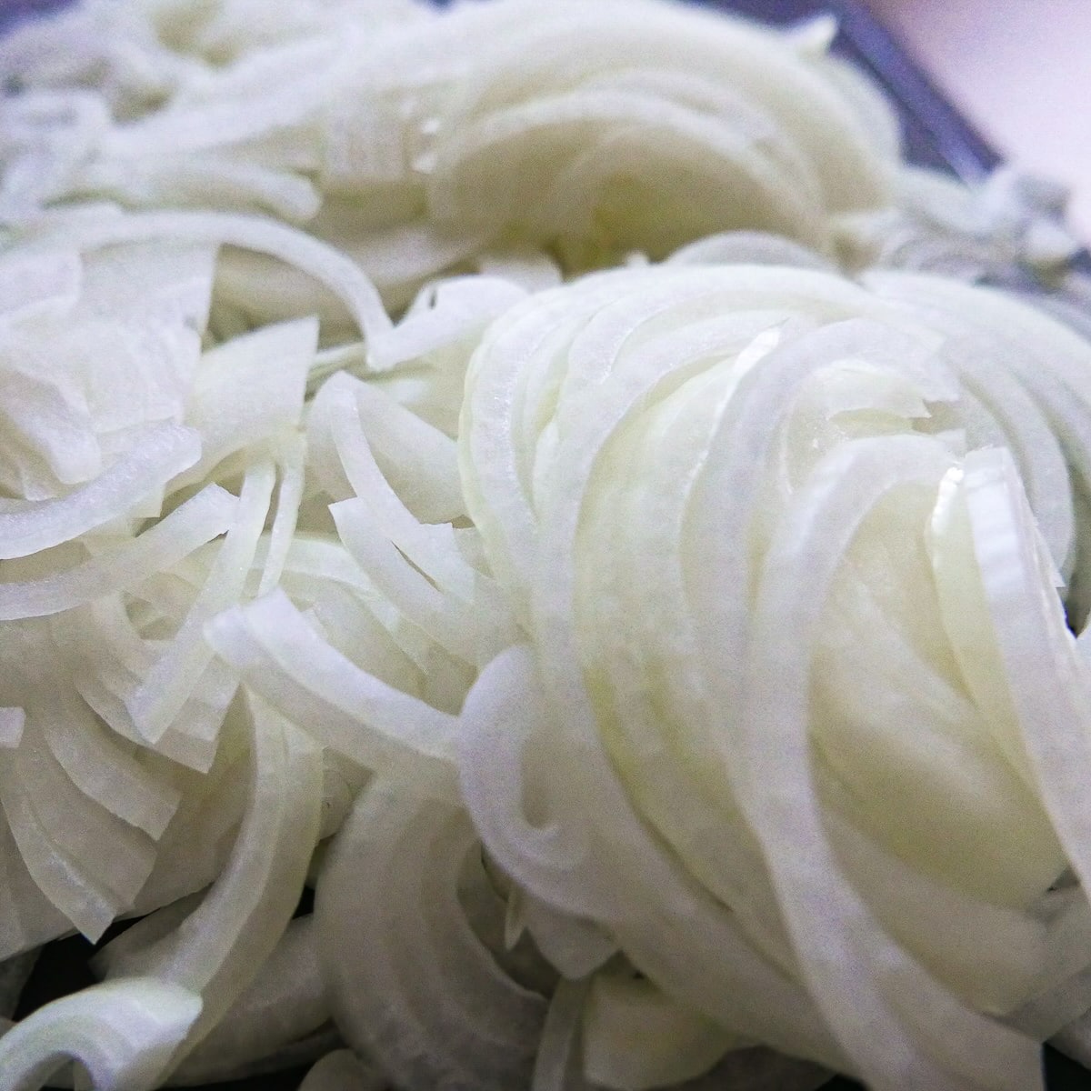 sliced-onions.jpg Peeled and thinly sliced onions on a cutting board.