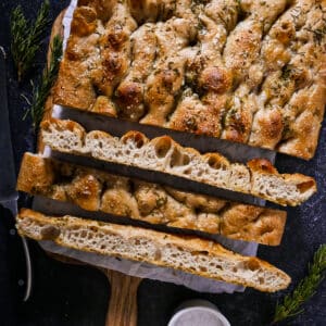Golden sourdough focaccia sliced into squares on parchment paper.