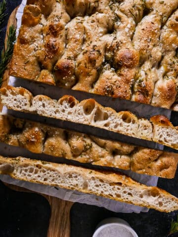 Golden sourdough focaccia sliced into squares on parchment paper.